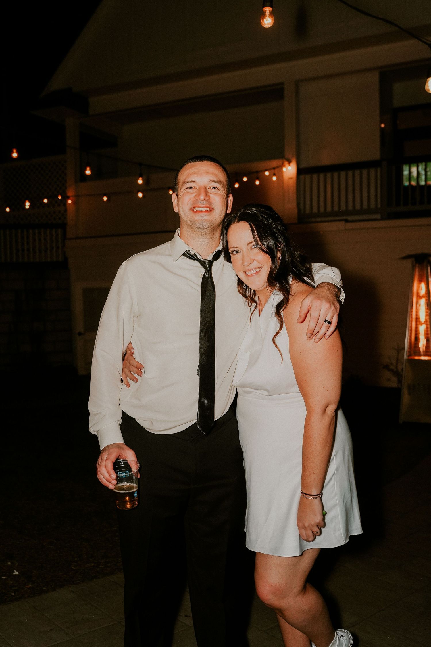 A couple shares a romantic moment on a dimly lit porch with string lights creating an intimate evening atmosphere.