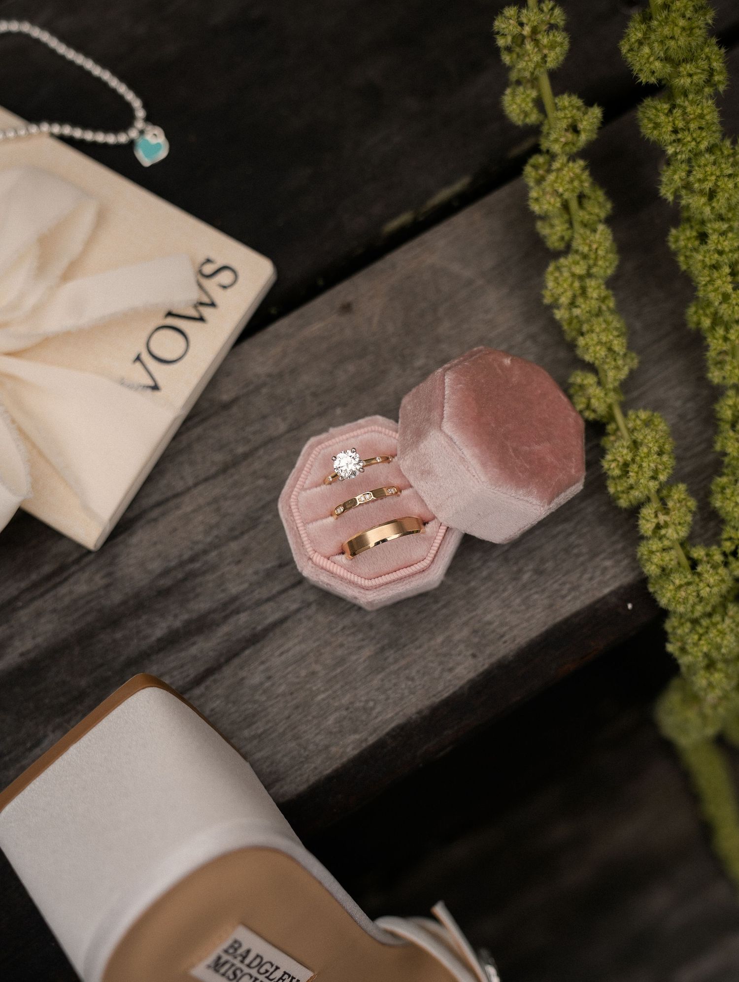Pink velvet ring box with wedding bands and diamond engagement ring on rustic wood surface.