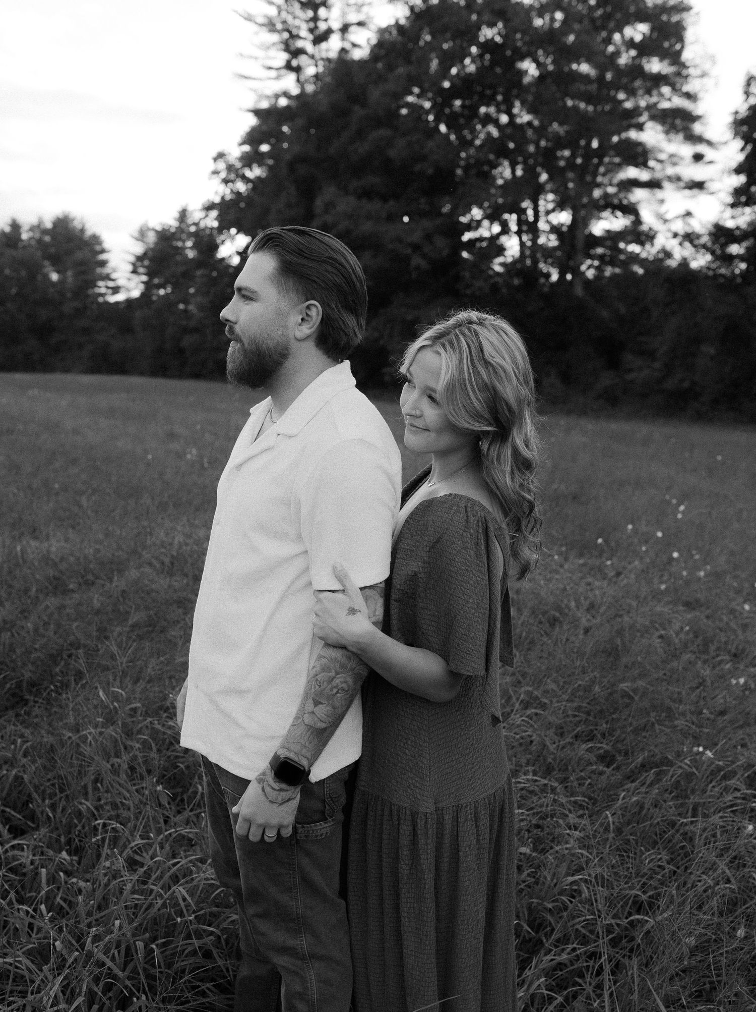 A couple stands together in a field at sunset sharing an intimate moment in black and white.