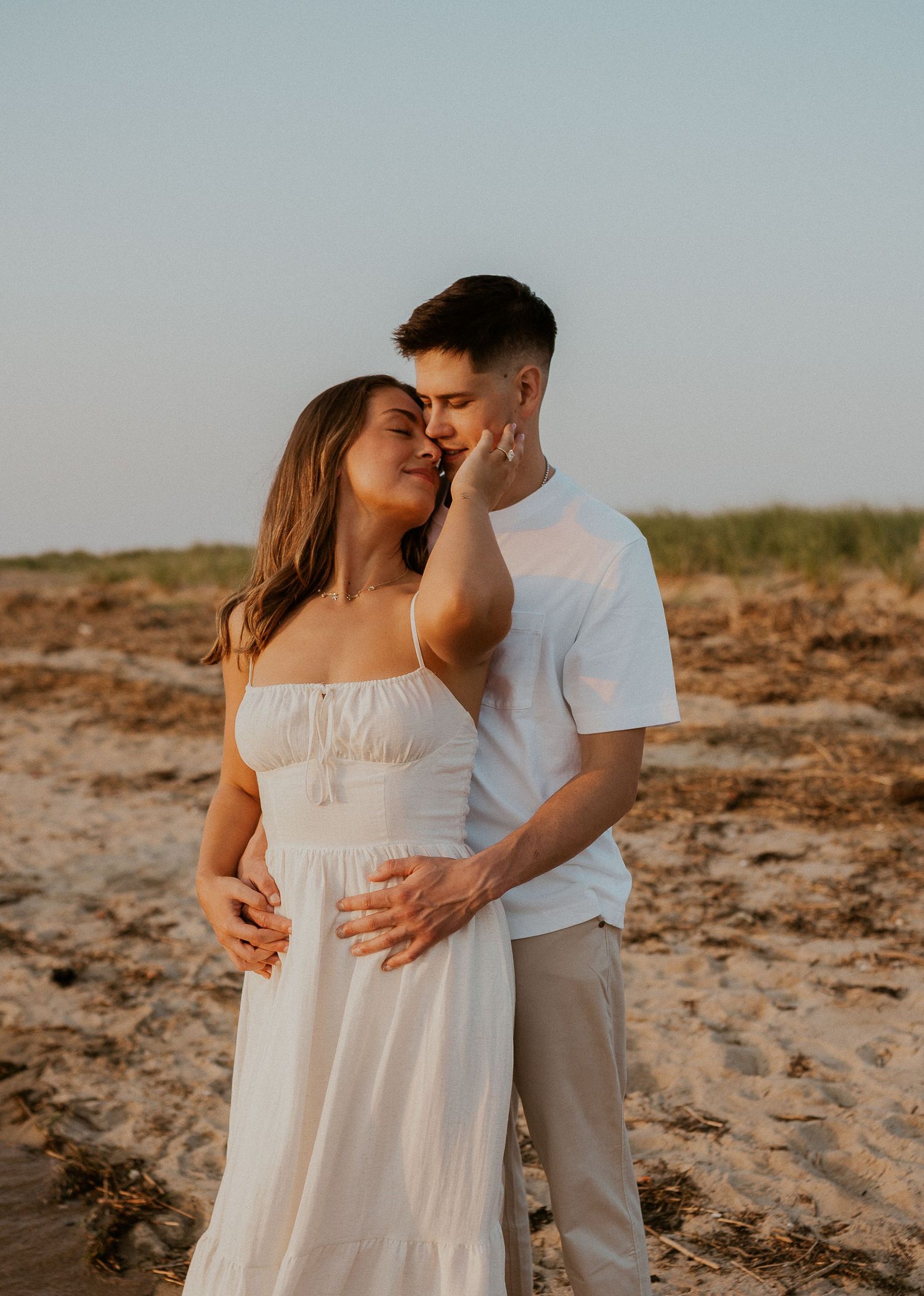 Loving couple in white outfits sharing an intimate moment on a beach during sunset.