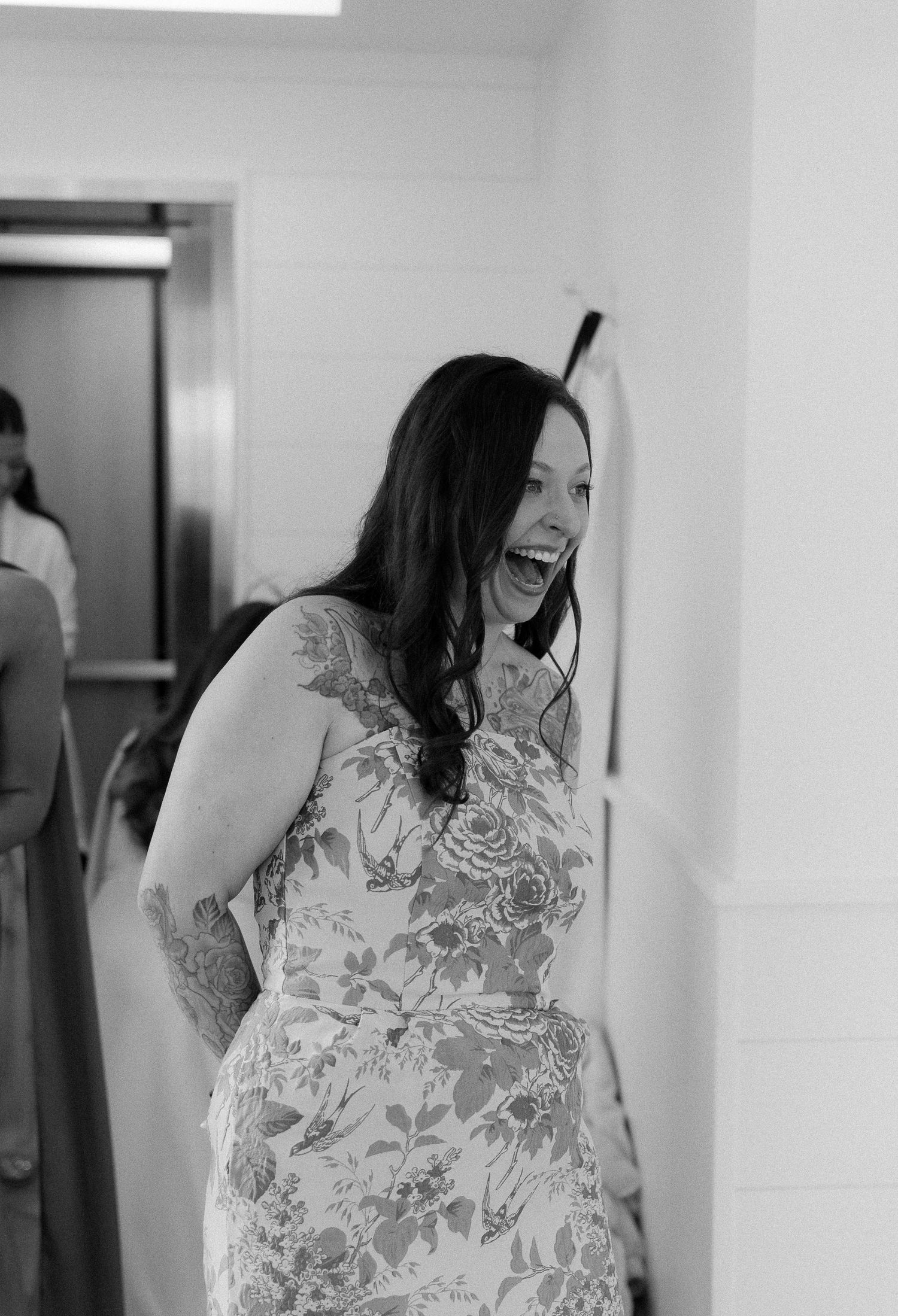 Woman in floral dress laughing joyfully during wedding preparations in black and white photo.