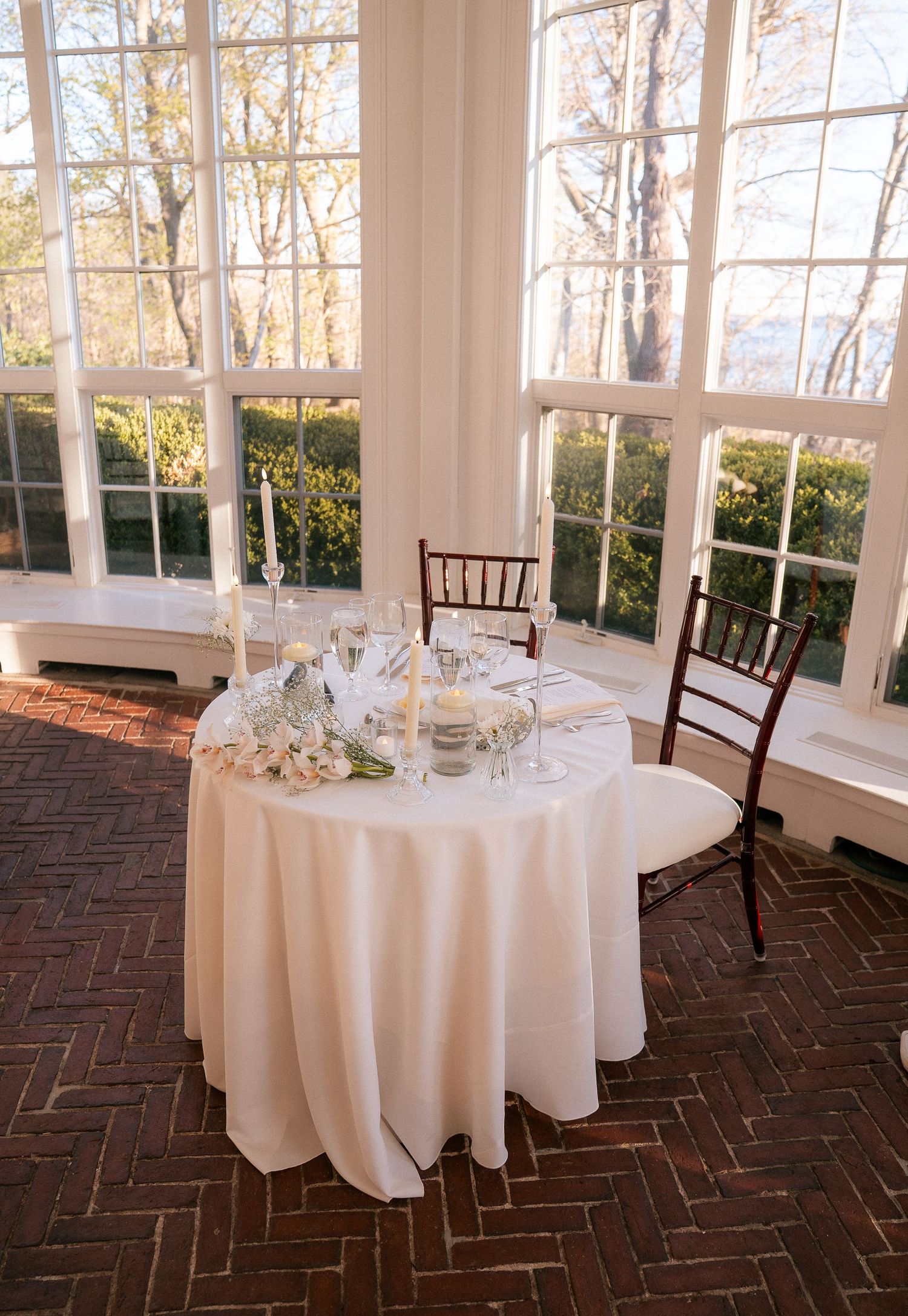 Intimate sweetheart table with white floral centerpiece and candles in a bright windowed wedding venue.