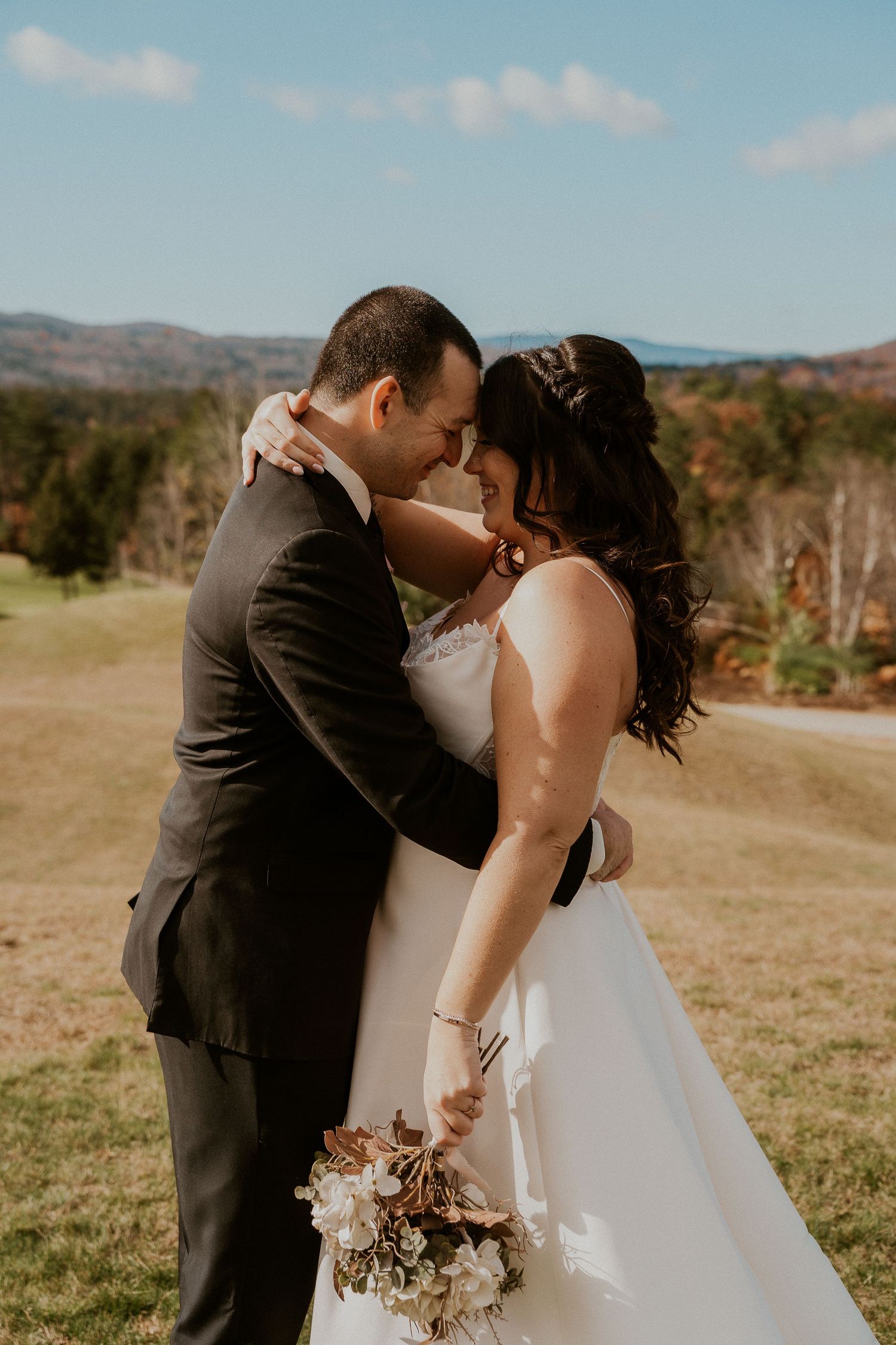 A romantic wedding moment captured outdoors with rolling hills and autumn scenery in the background.