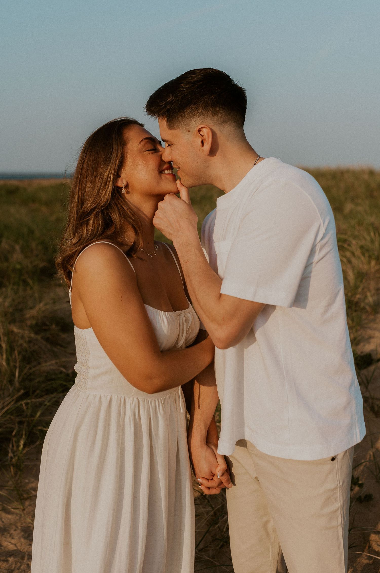 Sunset engagement session showing intimate moments between a couple in white outfits on sandy terrain.