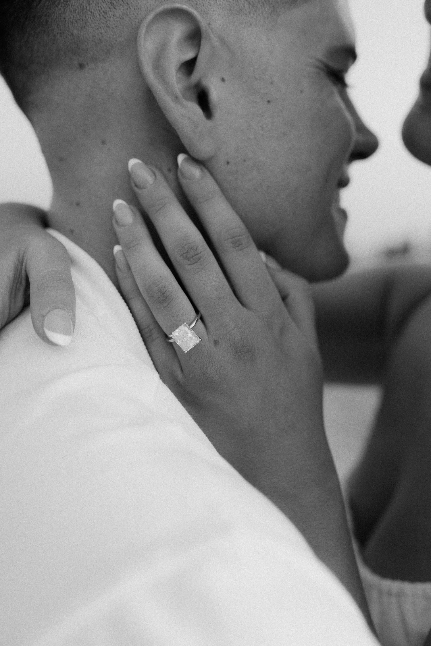 Close-up black and white shot of hand with engagement ring against white clothing.