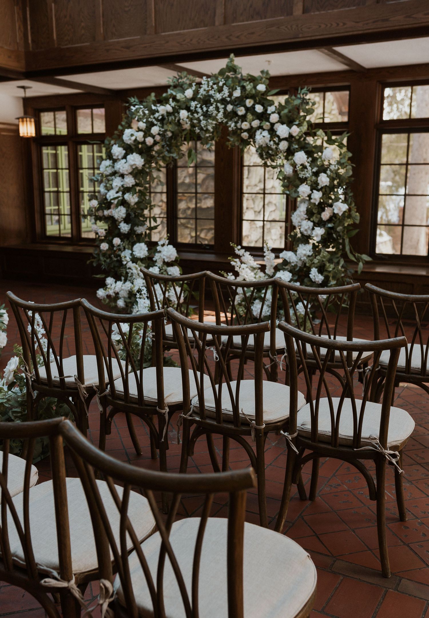 A wedding ceremony setup with bistro chairs and a floral arch in a rustic indoor venue.