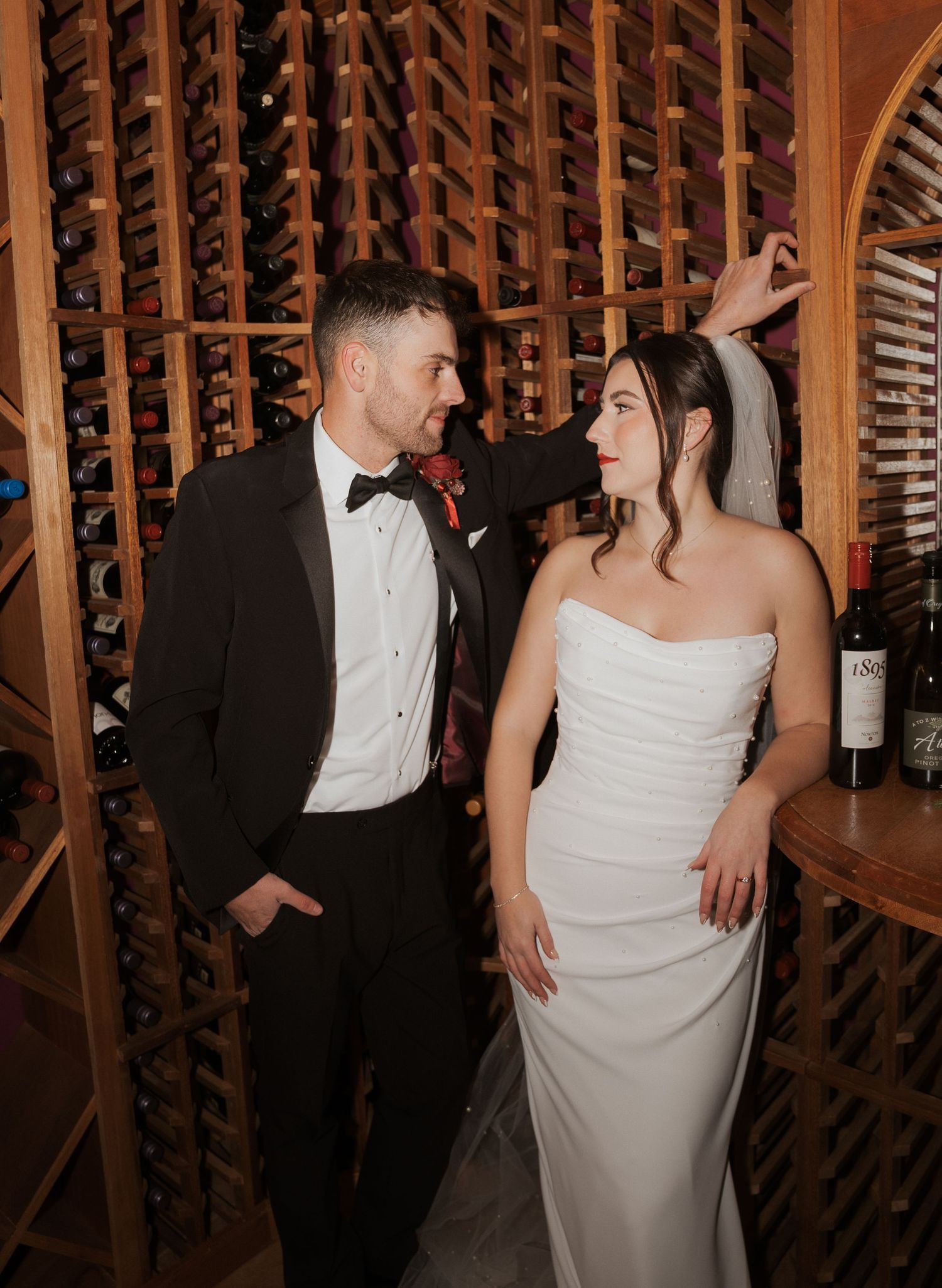 A couple shares a romantic moment in a wine cellar with wooden racks lining the walls.