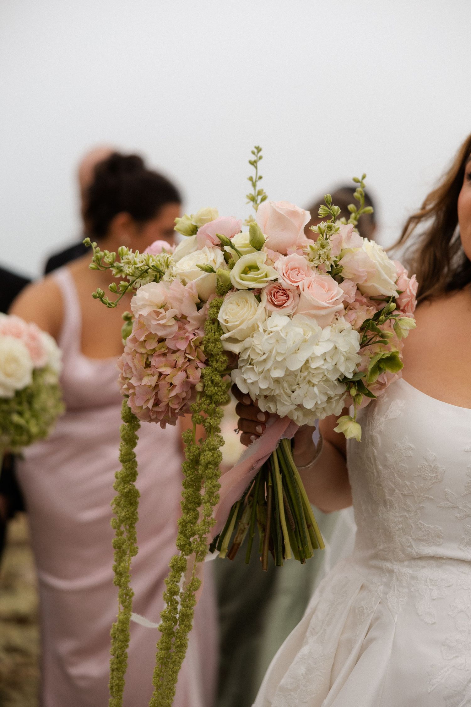 Close-up of bridal bouquet with pink roses, white hydrangeas, and cascading green amaranthus.