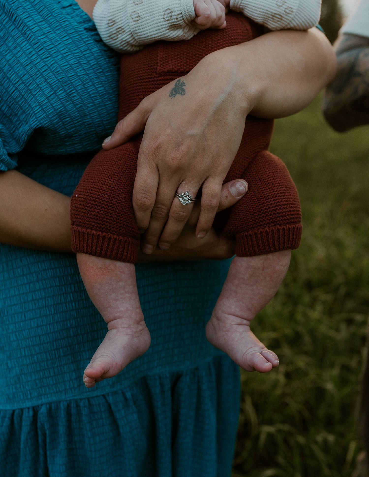 Close-up of hands holding baby's feet with engagement ring visible.