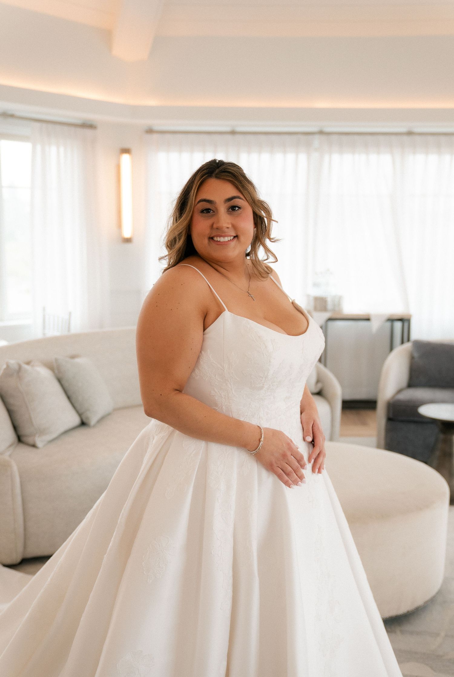 Smiling bride in a white spaghetti strap ballgown wedding dress poses in an elegant hotel suite.