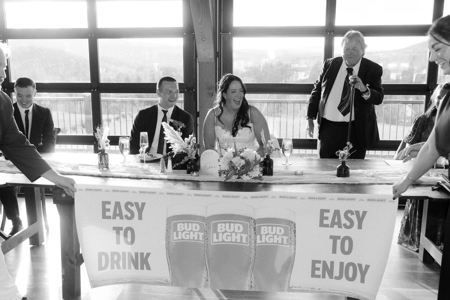 Black and white photo of Bud Light beer cans arranged in a row at a bar or restaurant counter.