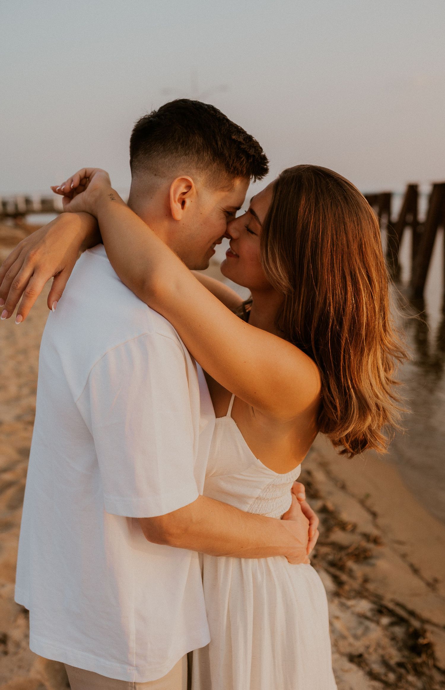 Intimate beach photoshoot of couple in white clothing during golden hour.