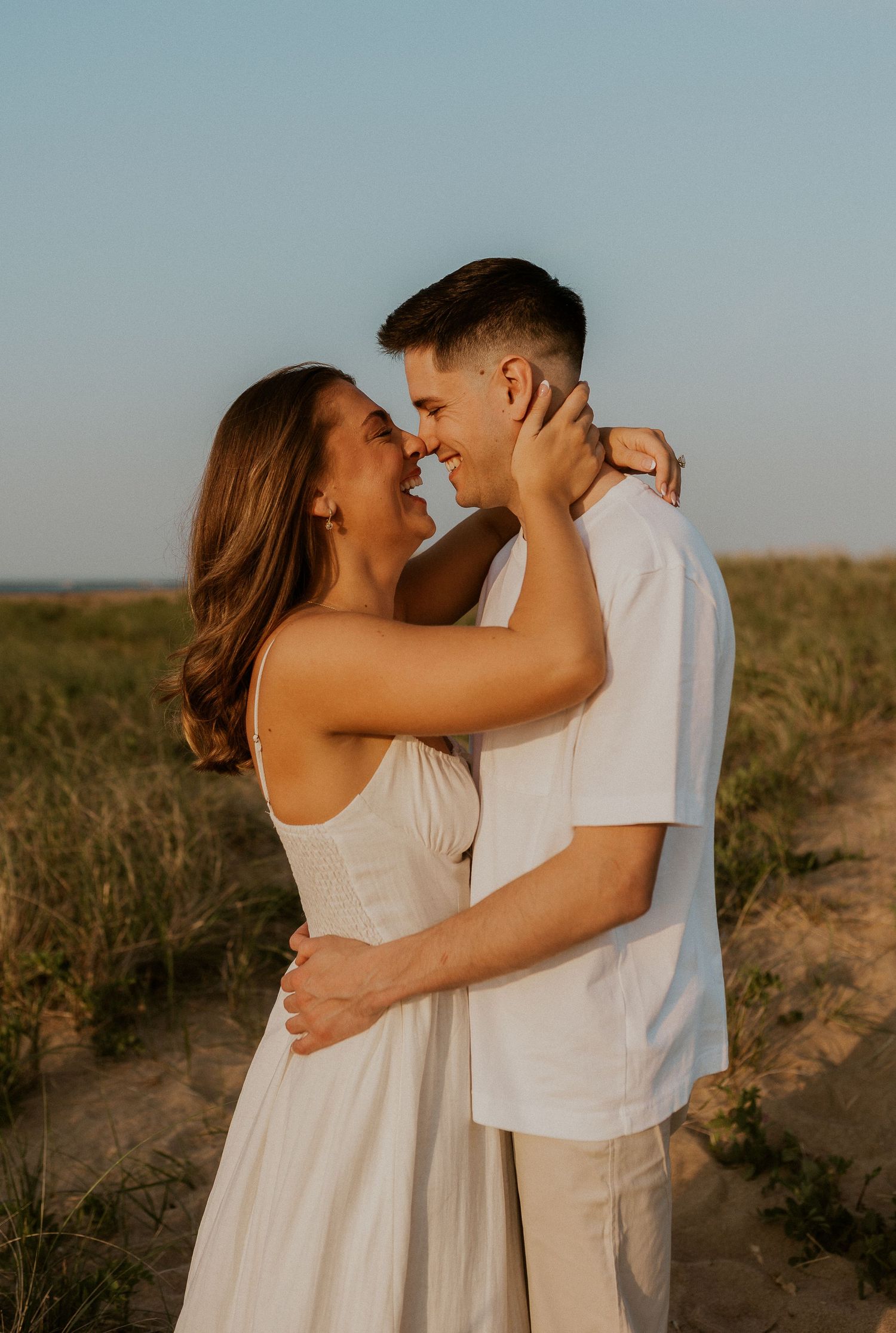 Romantic sunset portrait of couple embracing on grassy dunes.