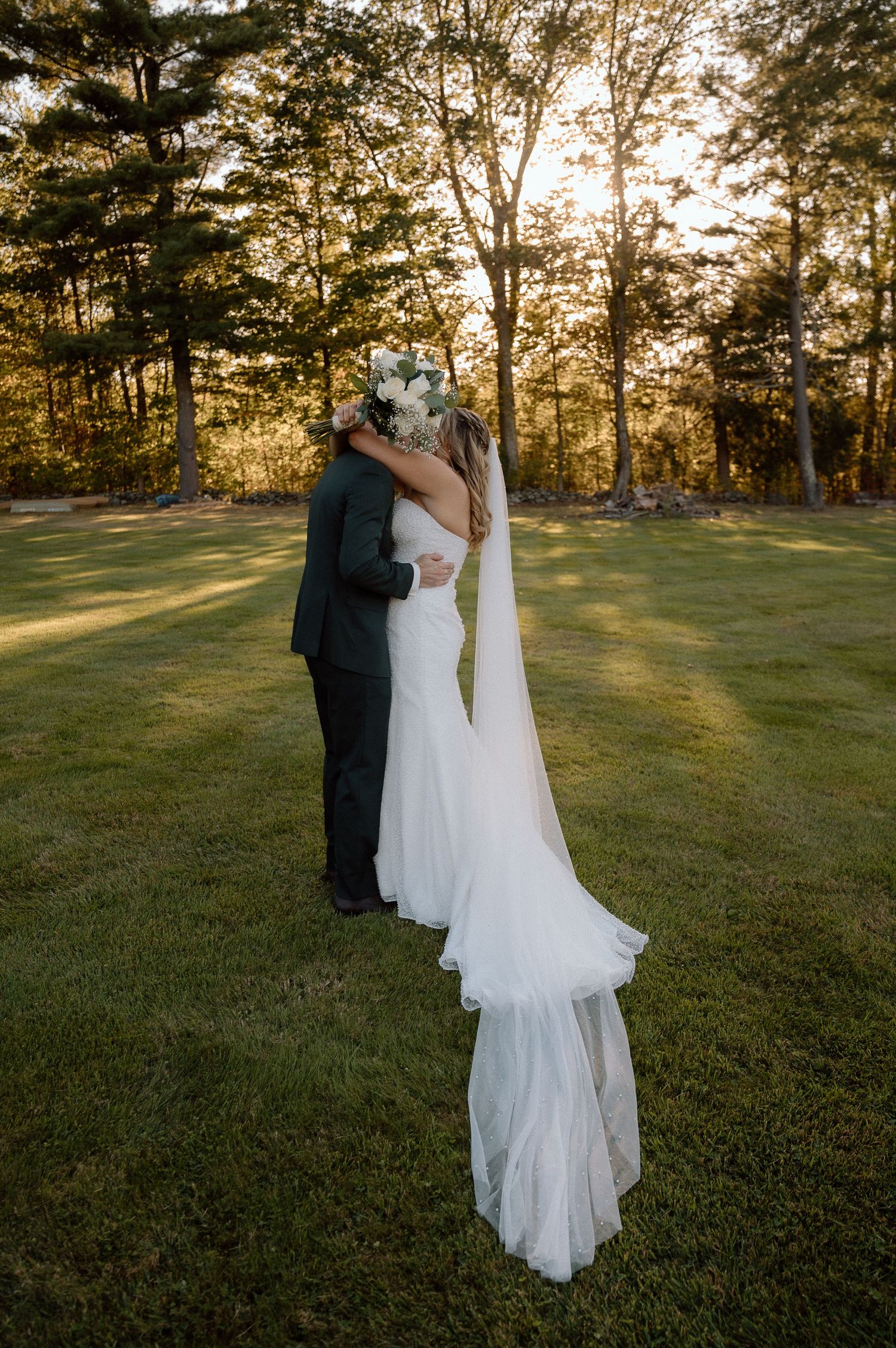 A romantic sunset wedding portrait with golden light filtering through trees in the background.