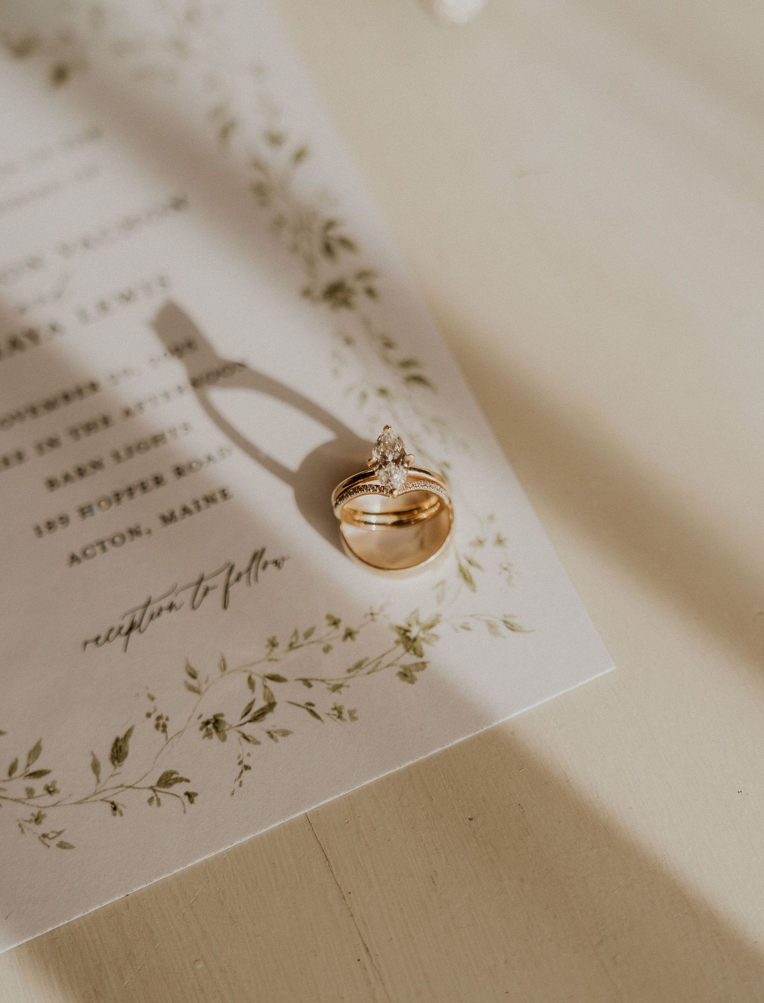 Gold wedding rings resting on a floral botanical wedding invitation on a cream surface.