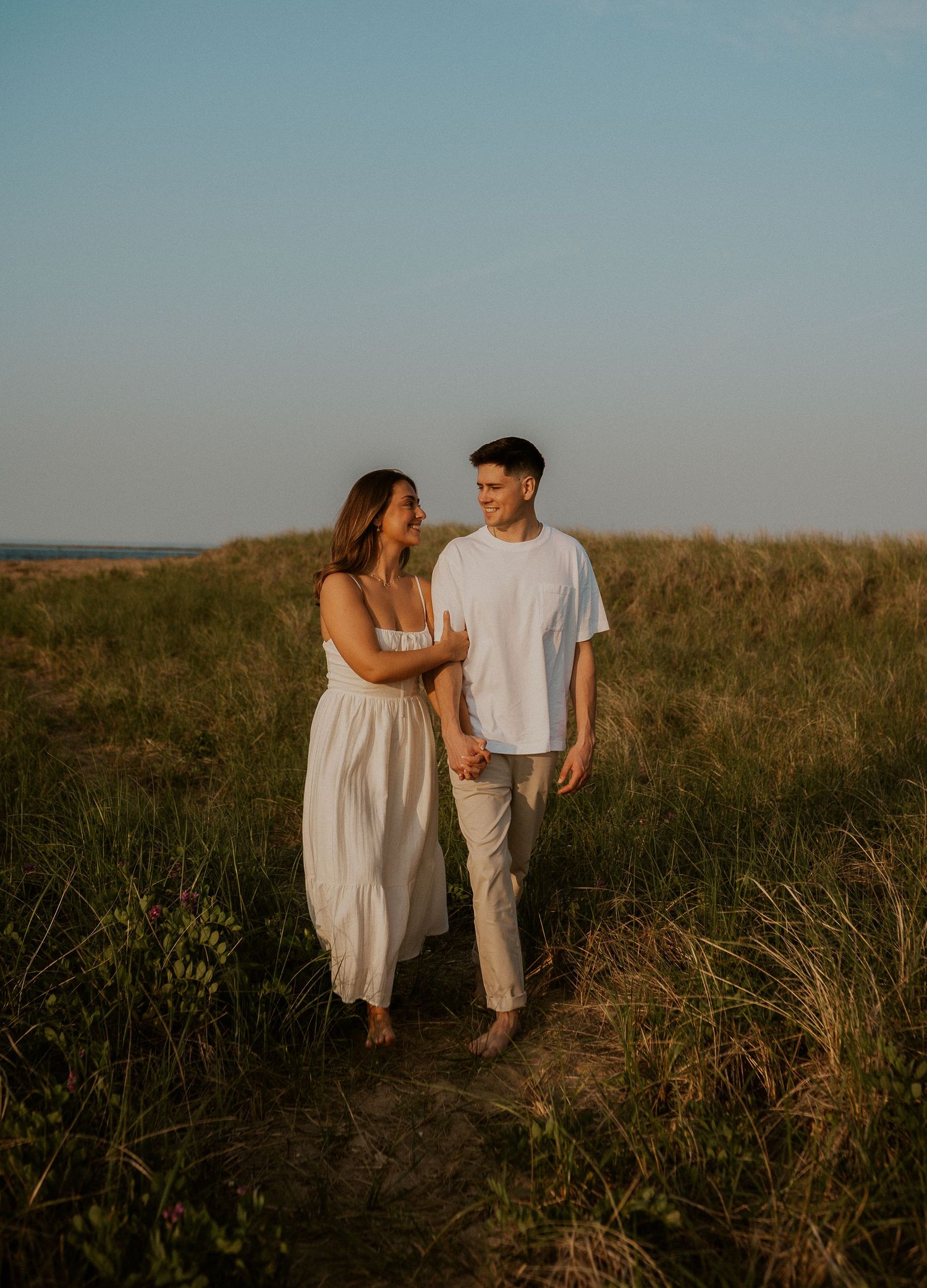 Couple walking together on sandy trail through coastal grassland.