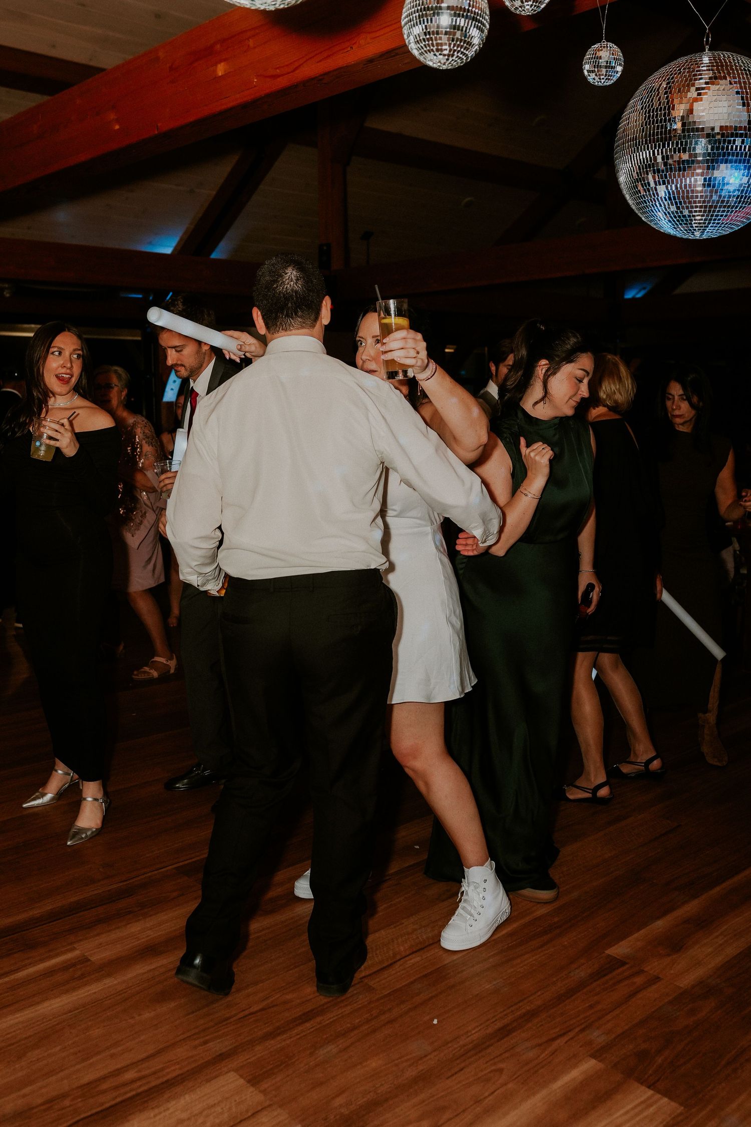 Wedding reception dance floor with disco balls overhead and guests dancing in a dimly lit room.