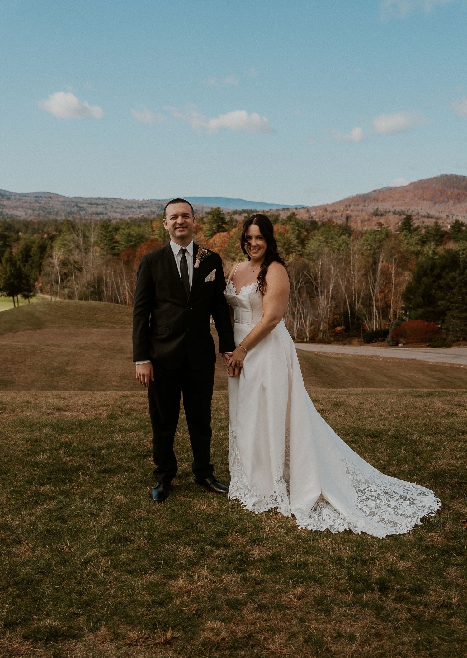 Couple poses together in a rustic outdoor setting with mountains and autumn trees in the background.