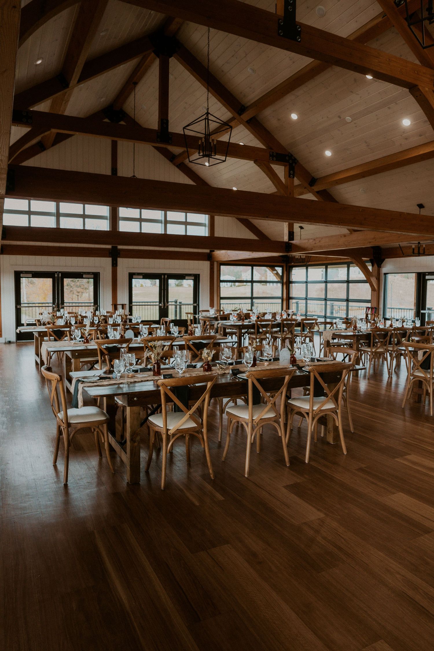 Elegant rustic wedding reception venue with exposed wooden beams and rows of tables set for dining.