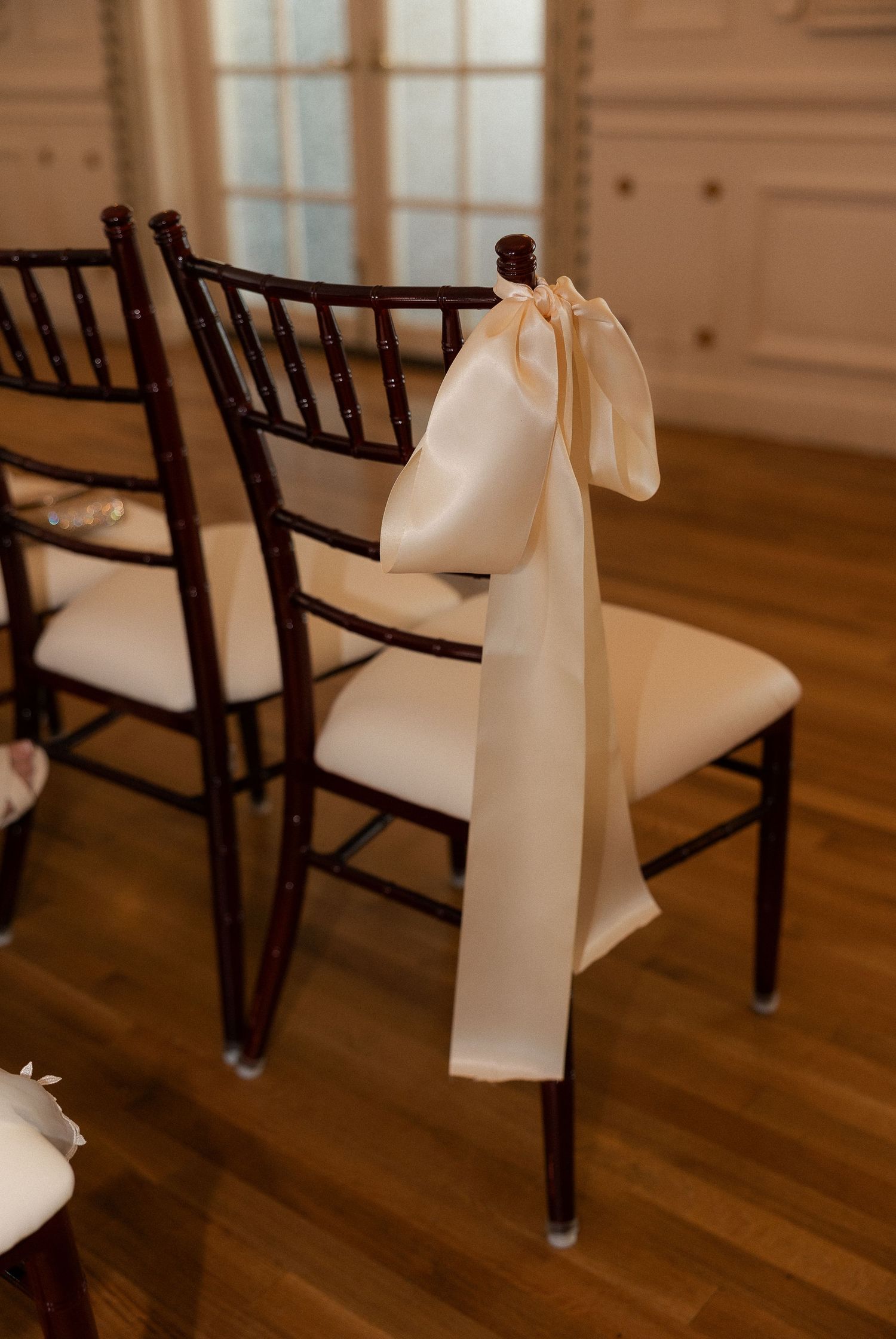 Elegant dark wood Chiavari chair with a long ivory satin ribbon bow tied to the back for a wedding ceremony.