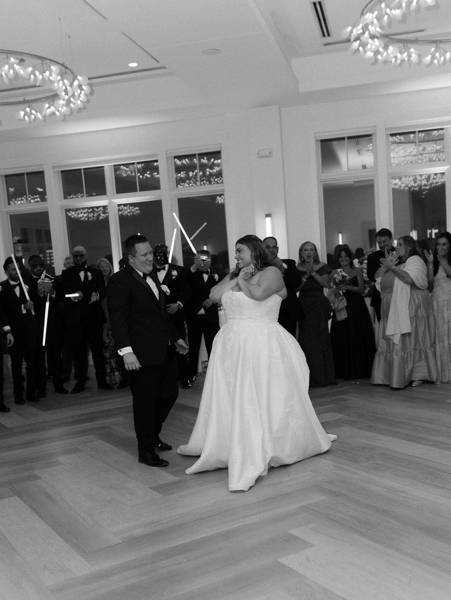 Bride and groom share their first dance at elegant wedding reception while guests watch and celebrate in black and white photo.