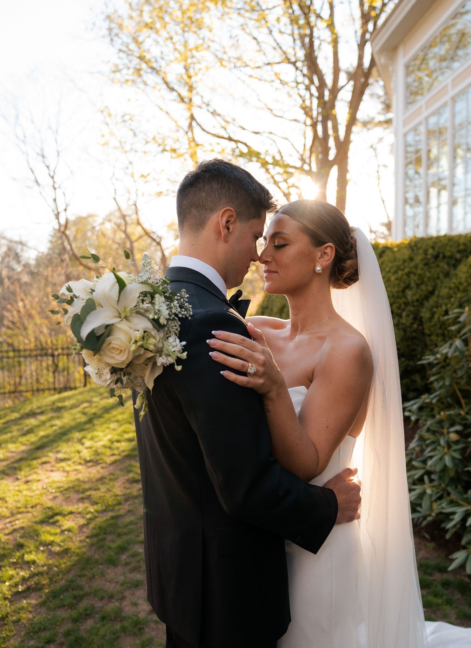 Bride and groom face each other in romantic golden hour light with white rose bouquet.