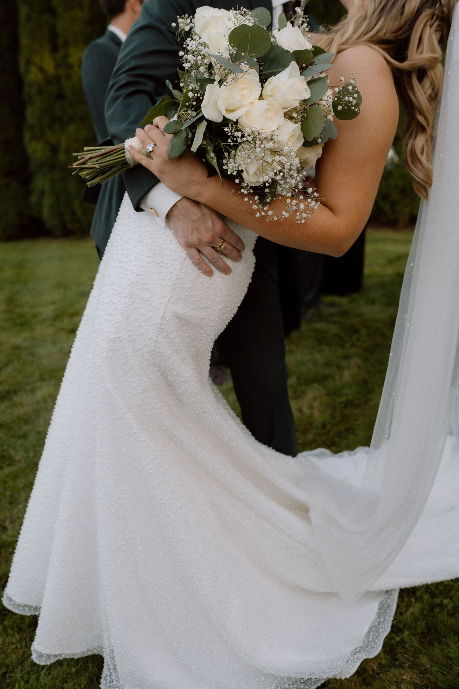 Detail shots of white wedding dress and bouquet featuring roses and baby's breath.