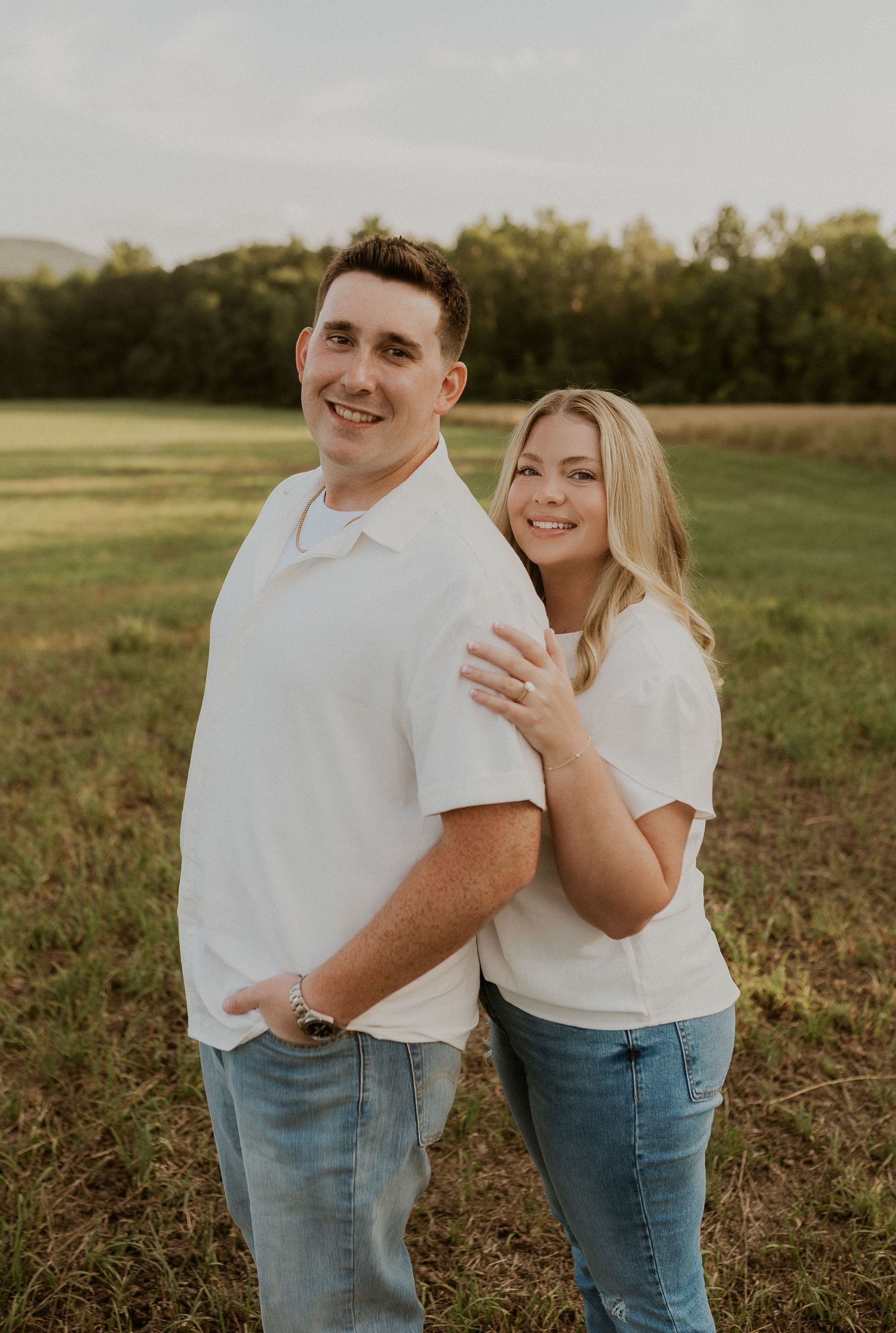 Couple wearing matching white tops and jeans laughing together in a field.