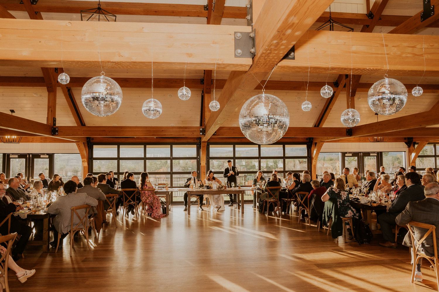 Rustic wedding reception venue with exposed wooden beams and hanging glass globe lights.