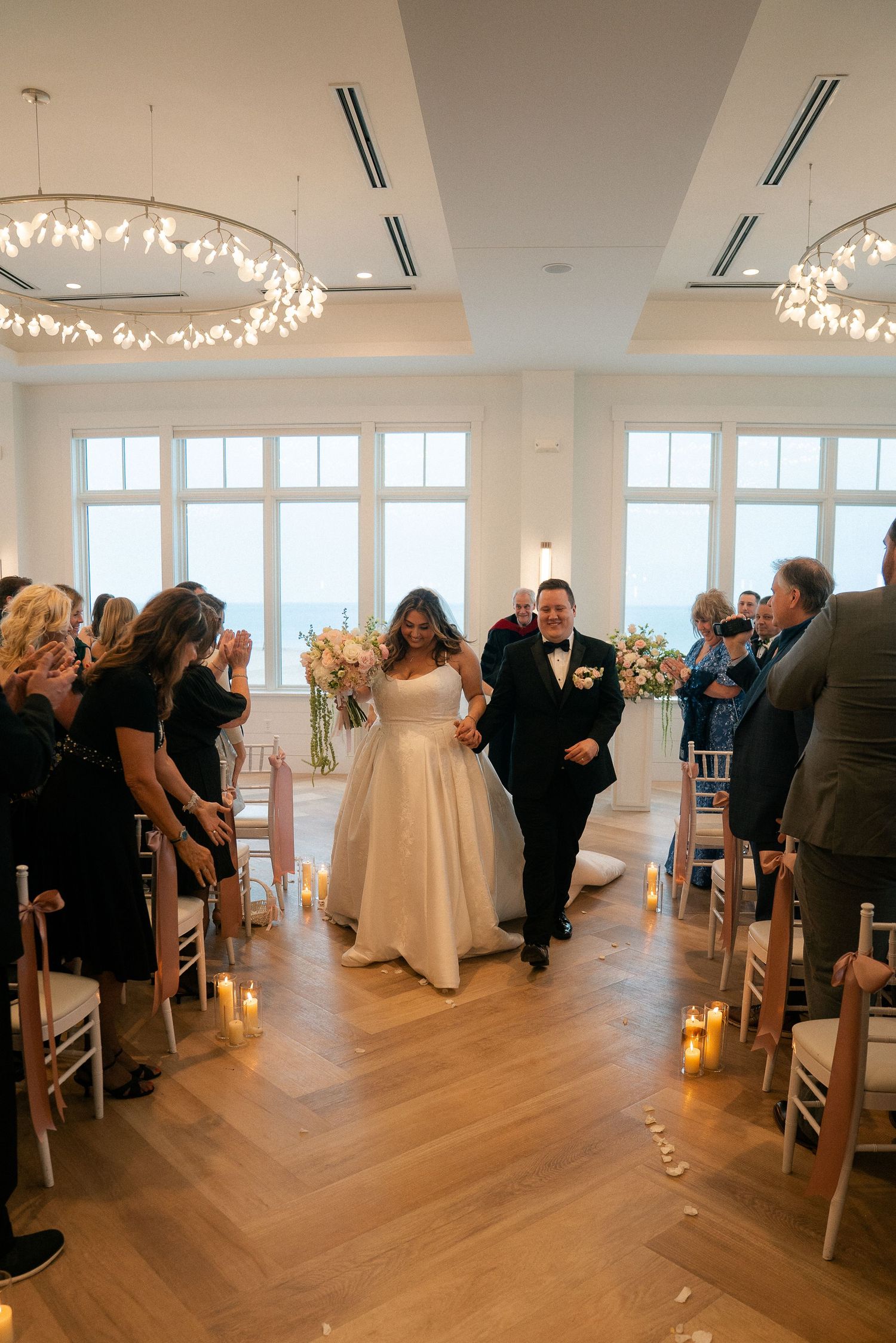 Newlyweds walk back down aisle hand in hand after wedding ceremony in bright elegant venue.