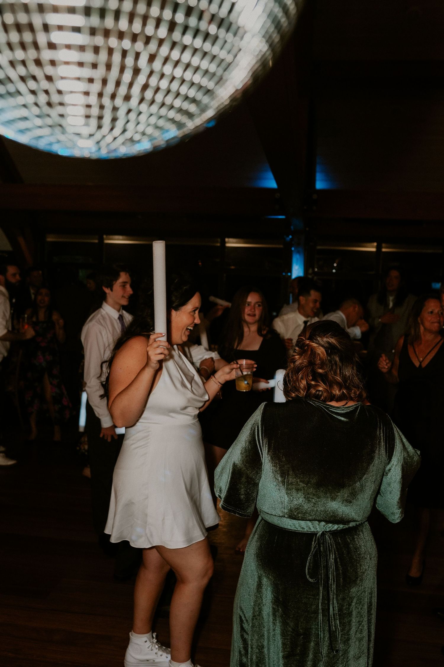 People dancing and celebrating at a dimly lit indoor party venue with decorative ceiling lights.