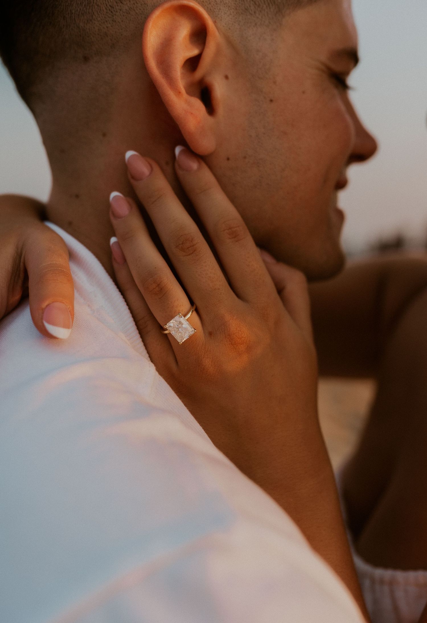 Side profile close-up showing hand with engagement ring against warm sunset lighting.