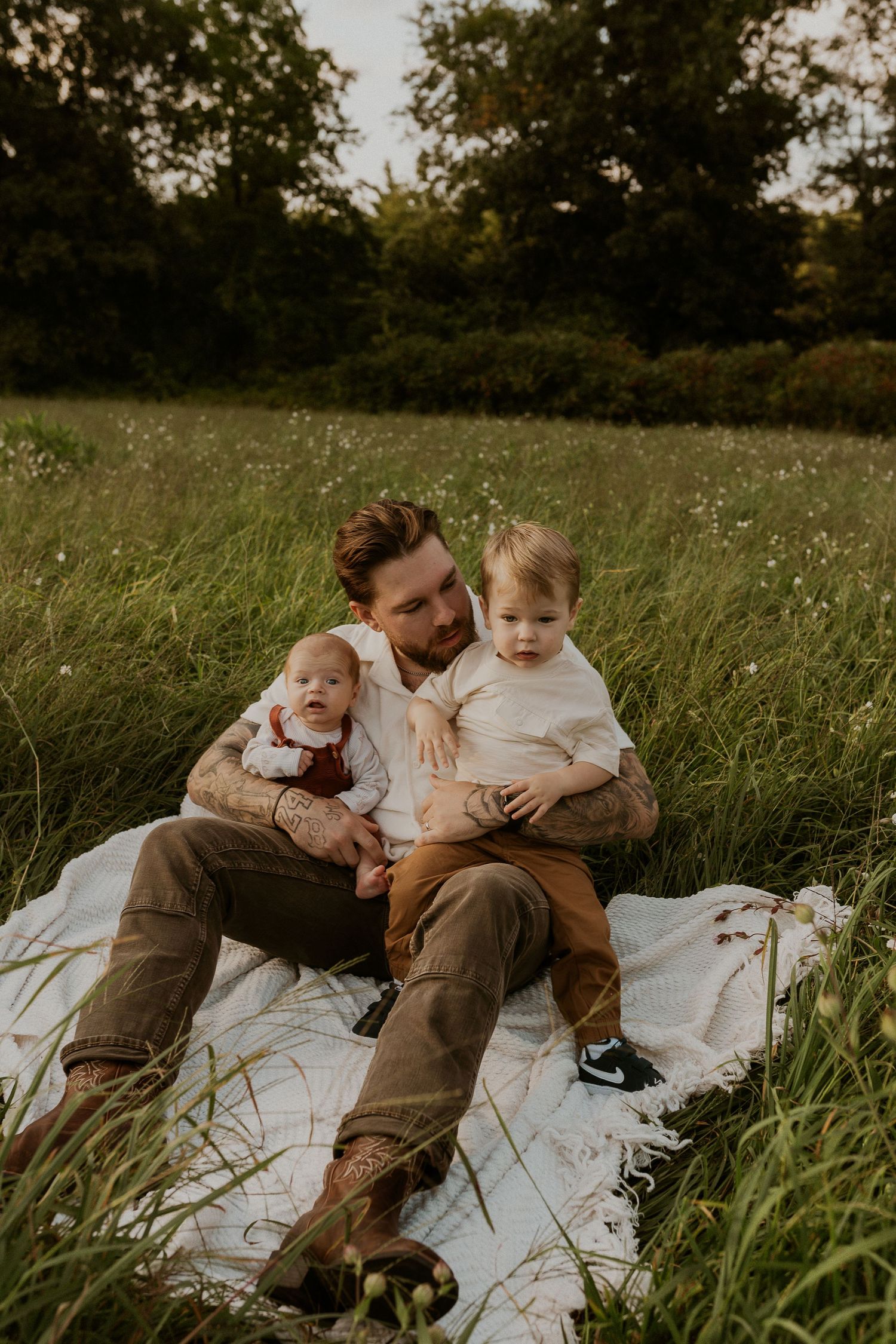 A family relaxes together on a white blanket in a grassy field during golden hour.