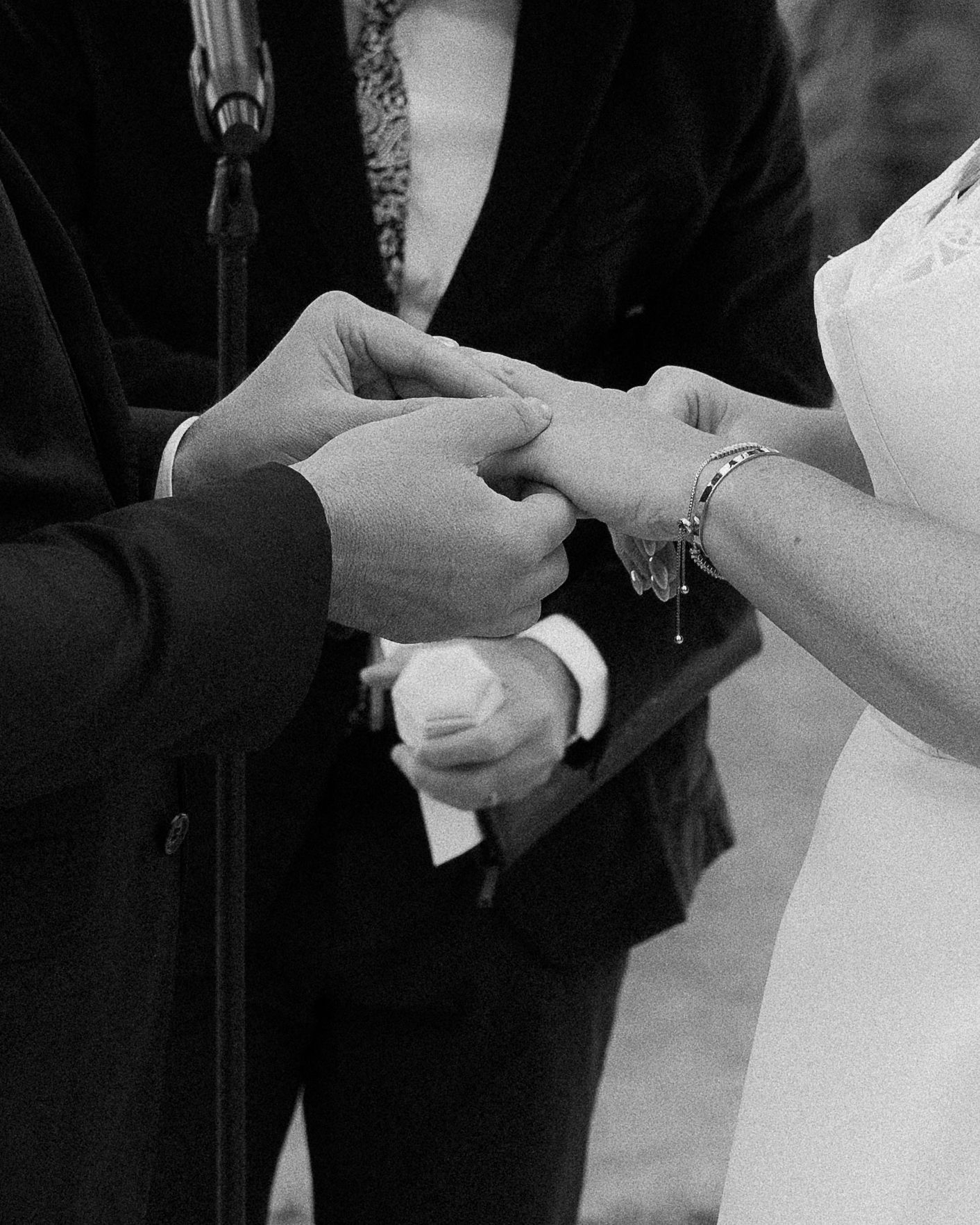 Close-up black and white photo of hands exchanging wedding rings during a marriage ceremony.