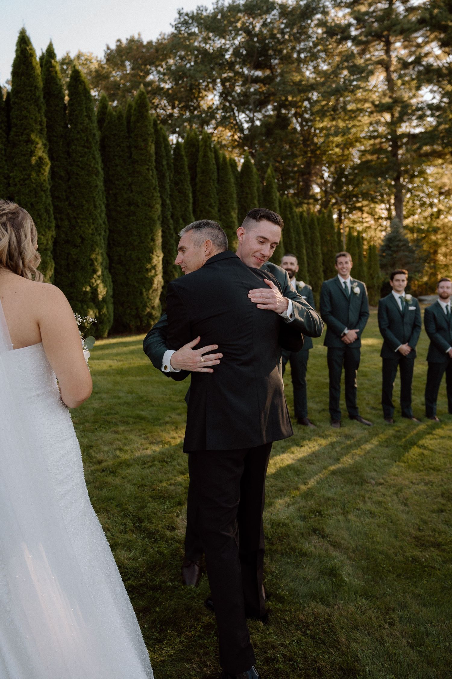 Emotional first look moment between bride and father at outdoor wedding ceremony with cypress trees in background.