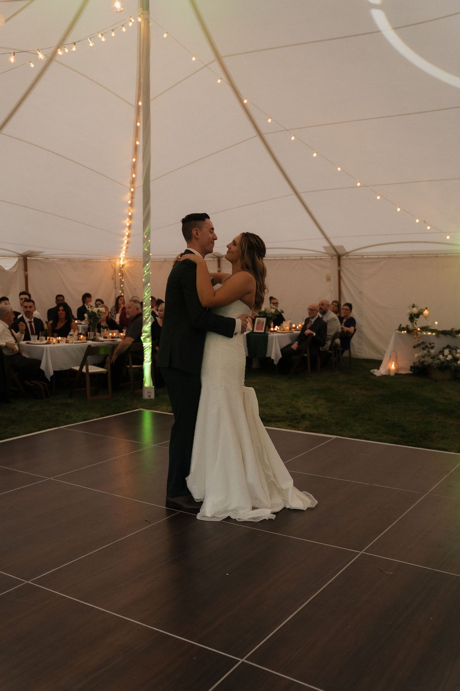 A couple embraces during their first dance at an outdoor tent wedding reception.