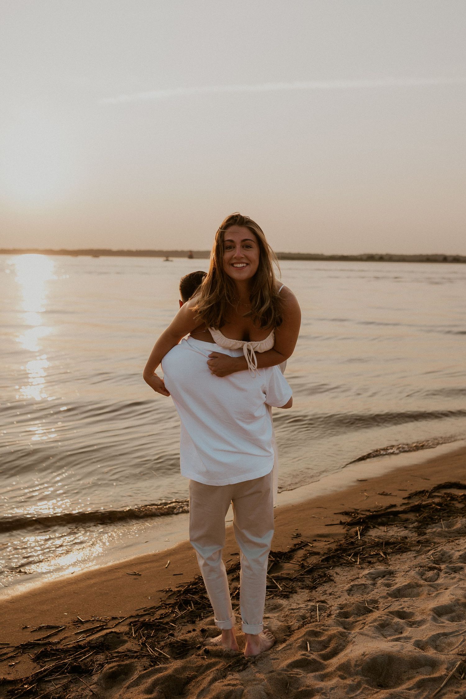 Playful piggyback ride on the beach at sunset with water and sand in the background.