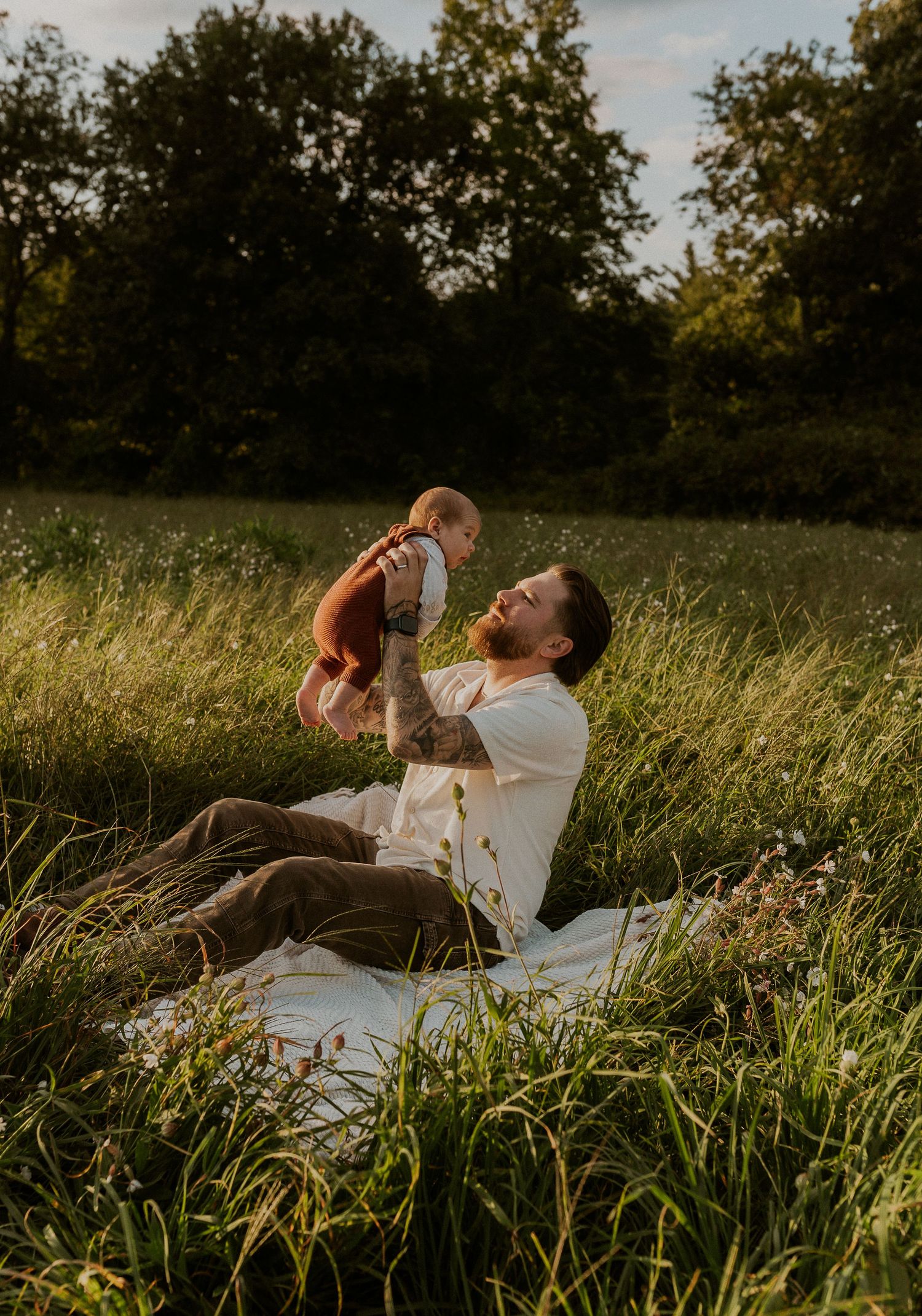 A couple relaxes in tall grass during golden hour while enjoying drinks together.