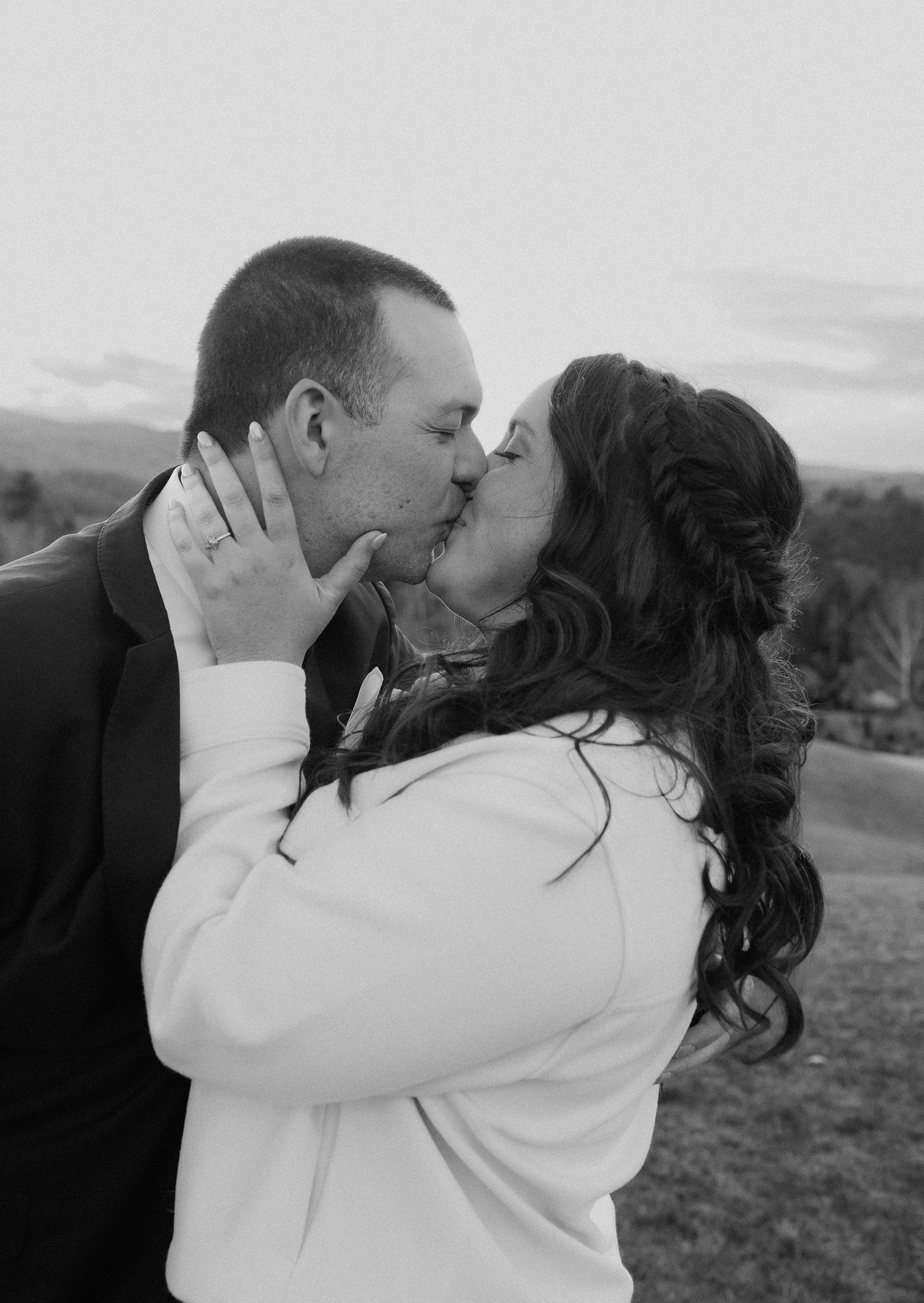 A romantic black and white photograph of a couple sharing an intimate kiss outdoors.