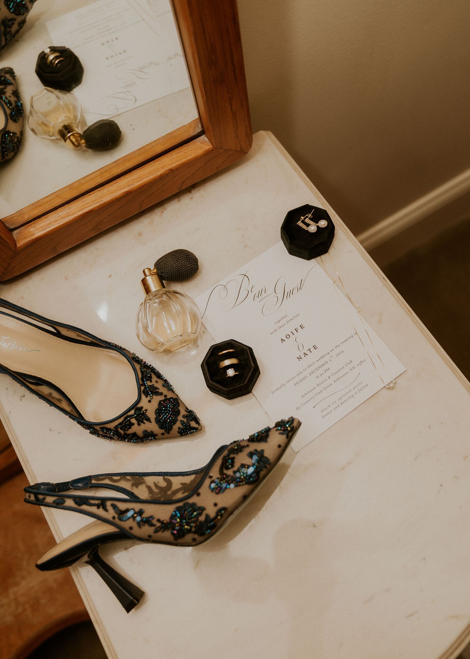 Elegant black lace heels with floral embroidery displayed on white paper with decorative black candles and stationery.