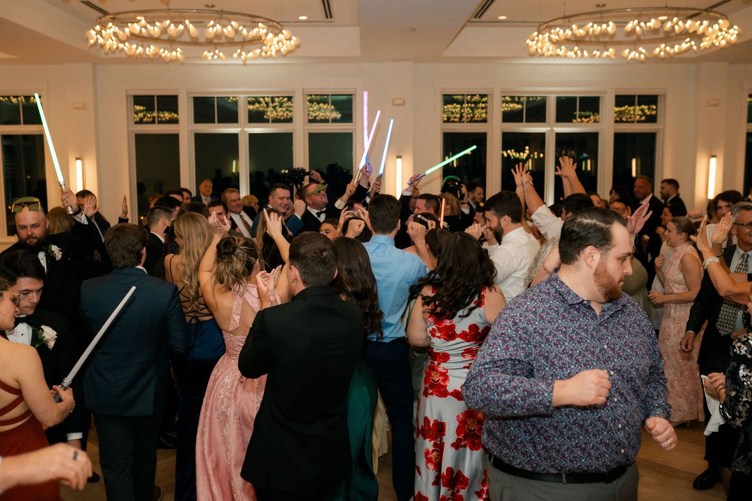 Guests dancing with light sabers at a lively wedding reception in an elegant ballroom venue.