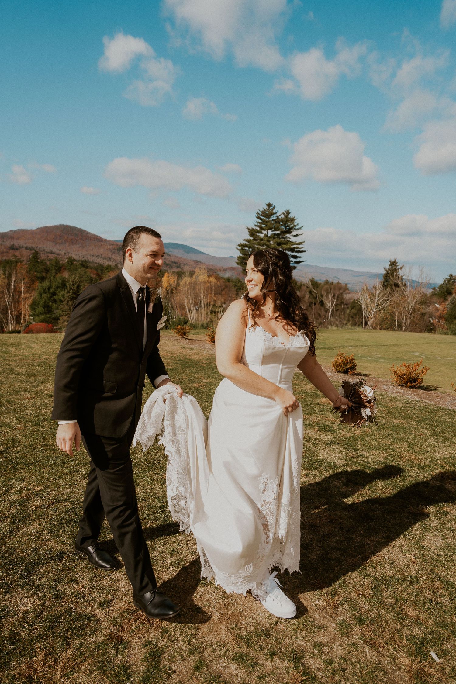 Playful wedding portraits in a sunny field with mountains and blue skies as backdrop.