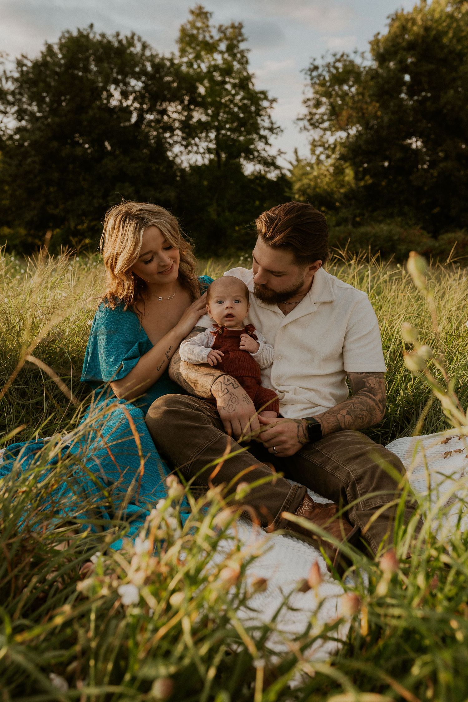 Family sharing tender moments while sitting together in a golden field at sunset.