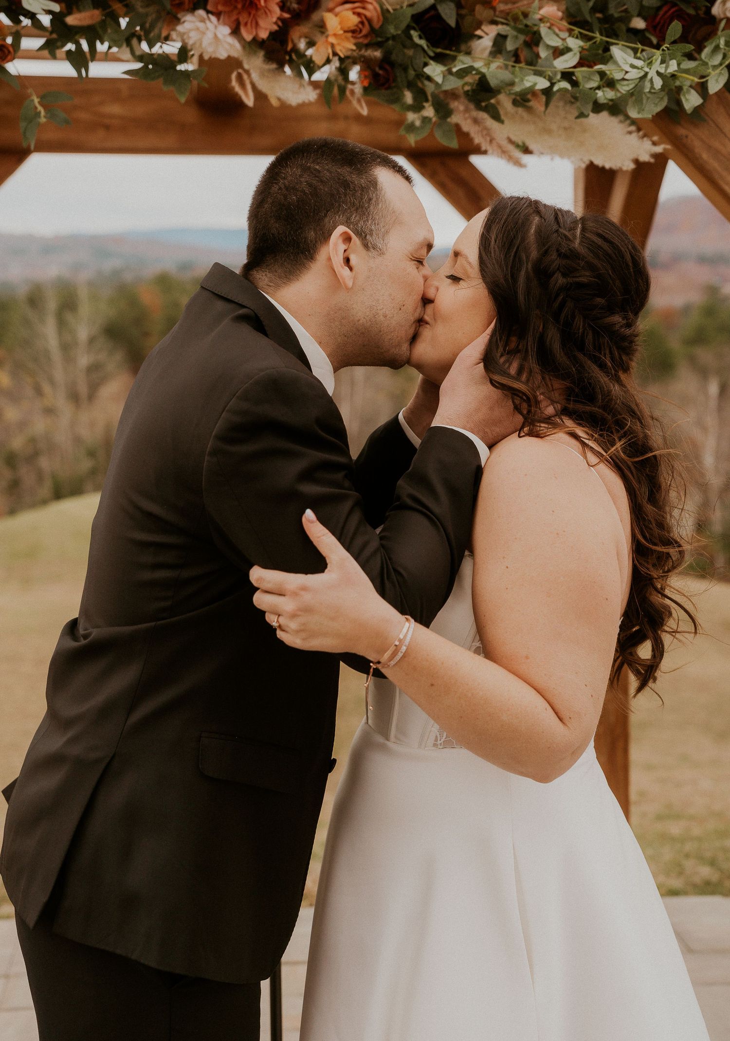 A romantic wedding kiss under floral decorations with mountain views in the background.
