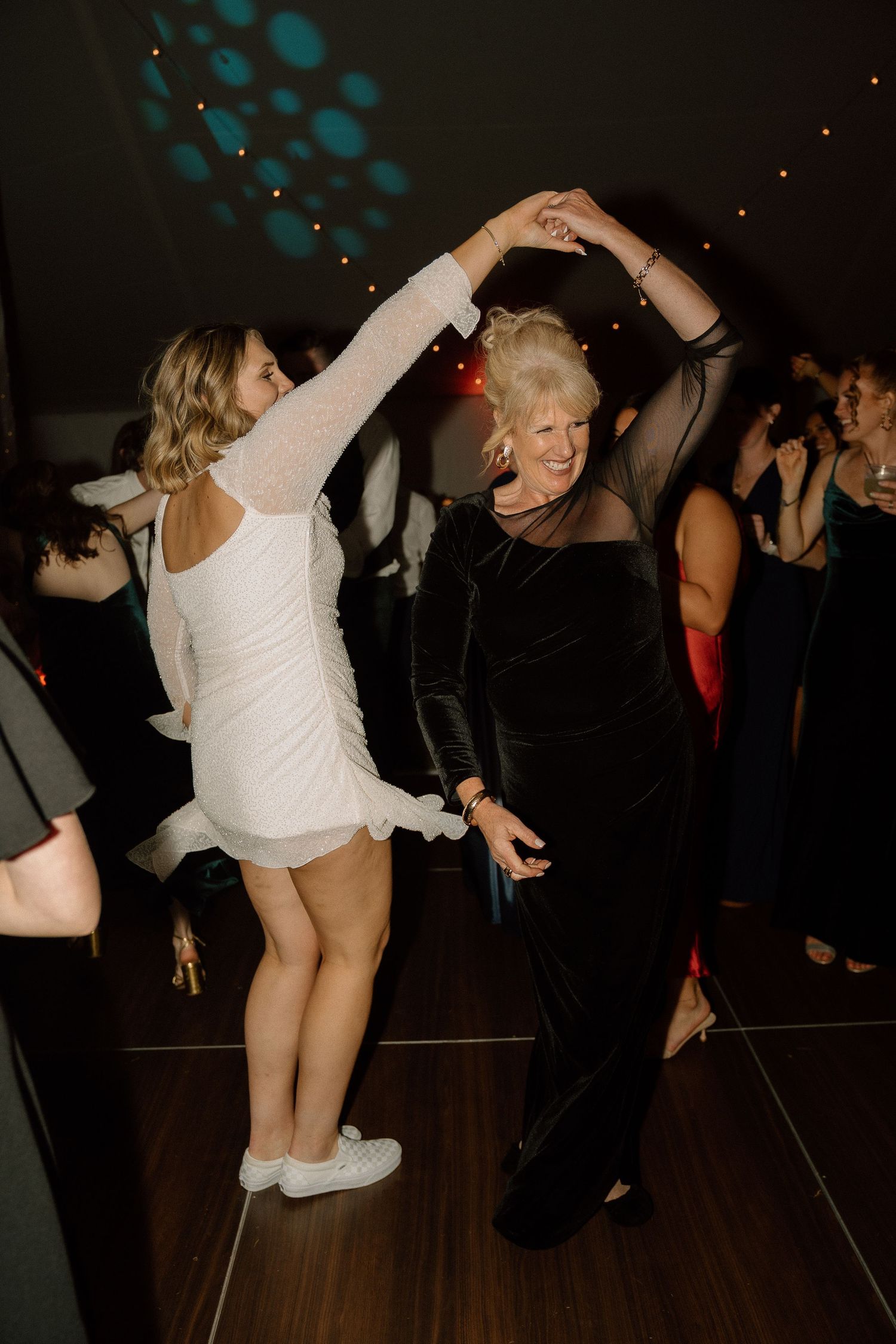 People dancing energetically at a dimly lit wedding reception with teal lighting accents.