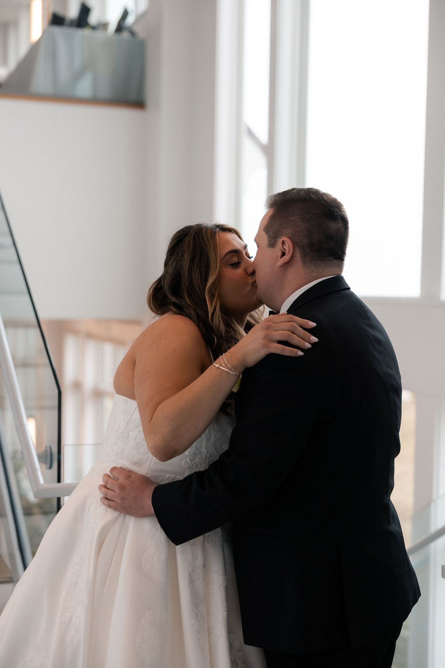 Bride and groom share a romantic kiss on a staircase, bride in white gown and groom in dark suit.