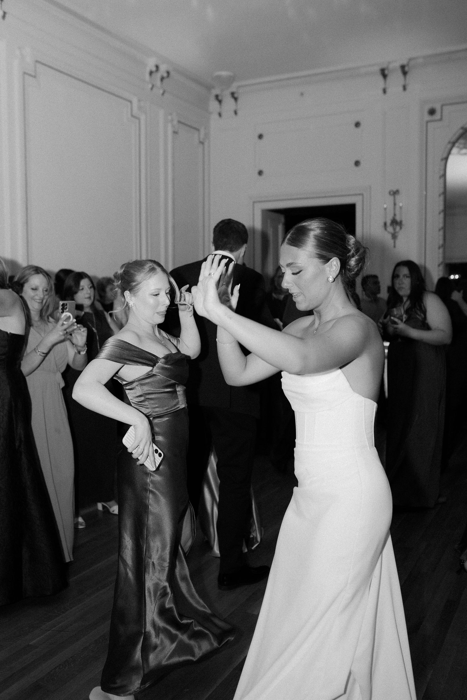 Bride in white strapless gown dancing with guest in satin dress at elegant black and white wedding reception.