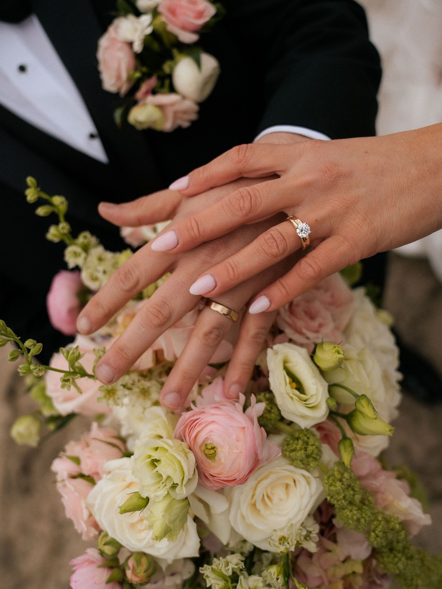 Bride and groom display wedding rings over pink and white floral bouquet closeup detail shot.