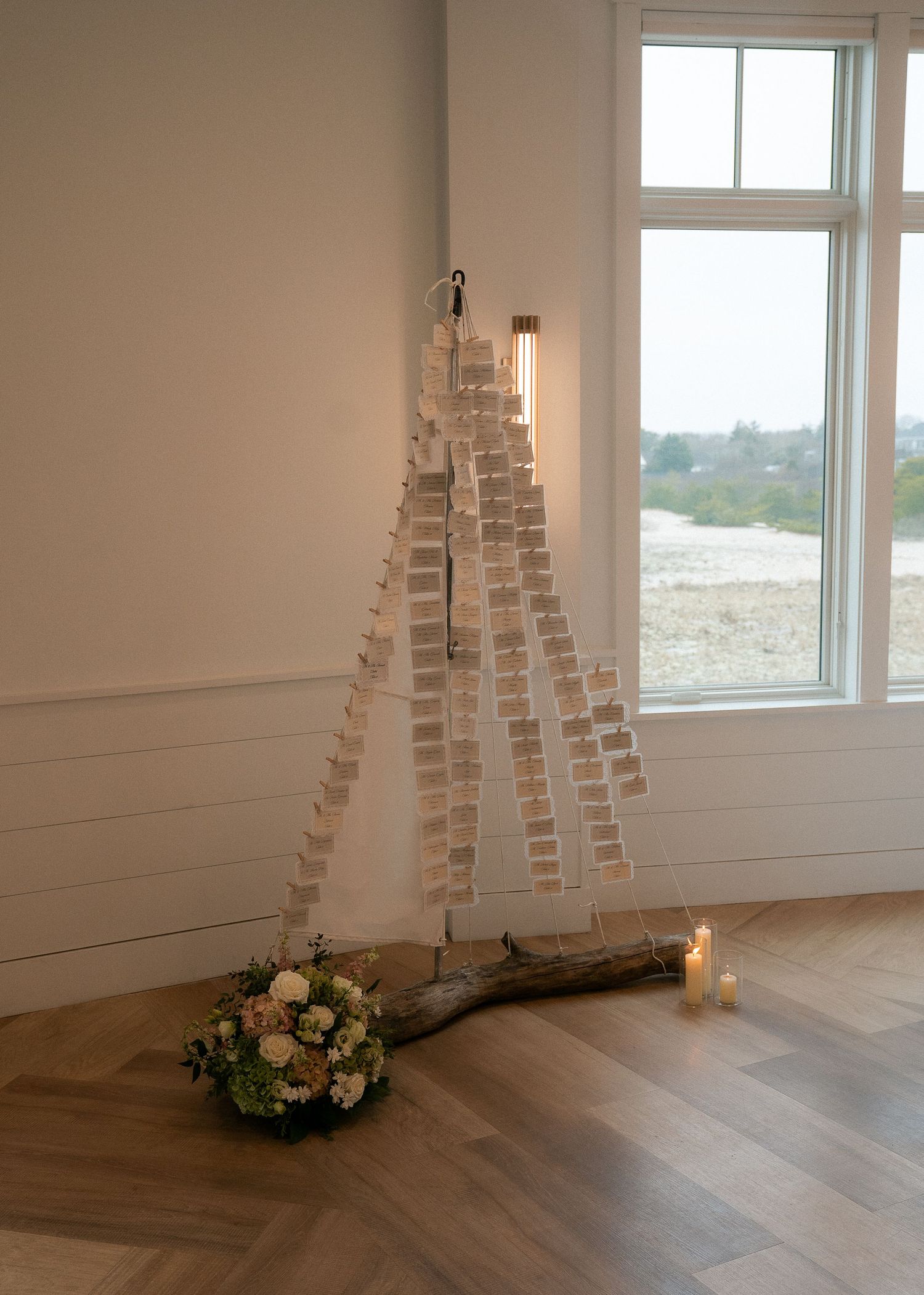 Rustic wedding seating chart display using wooden branch with escort cards, candles, and floral arrangement.