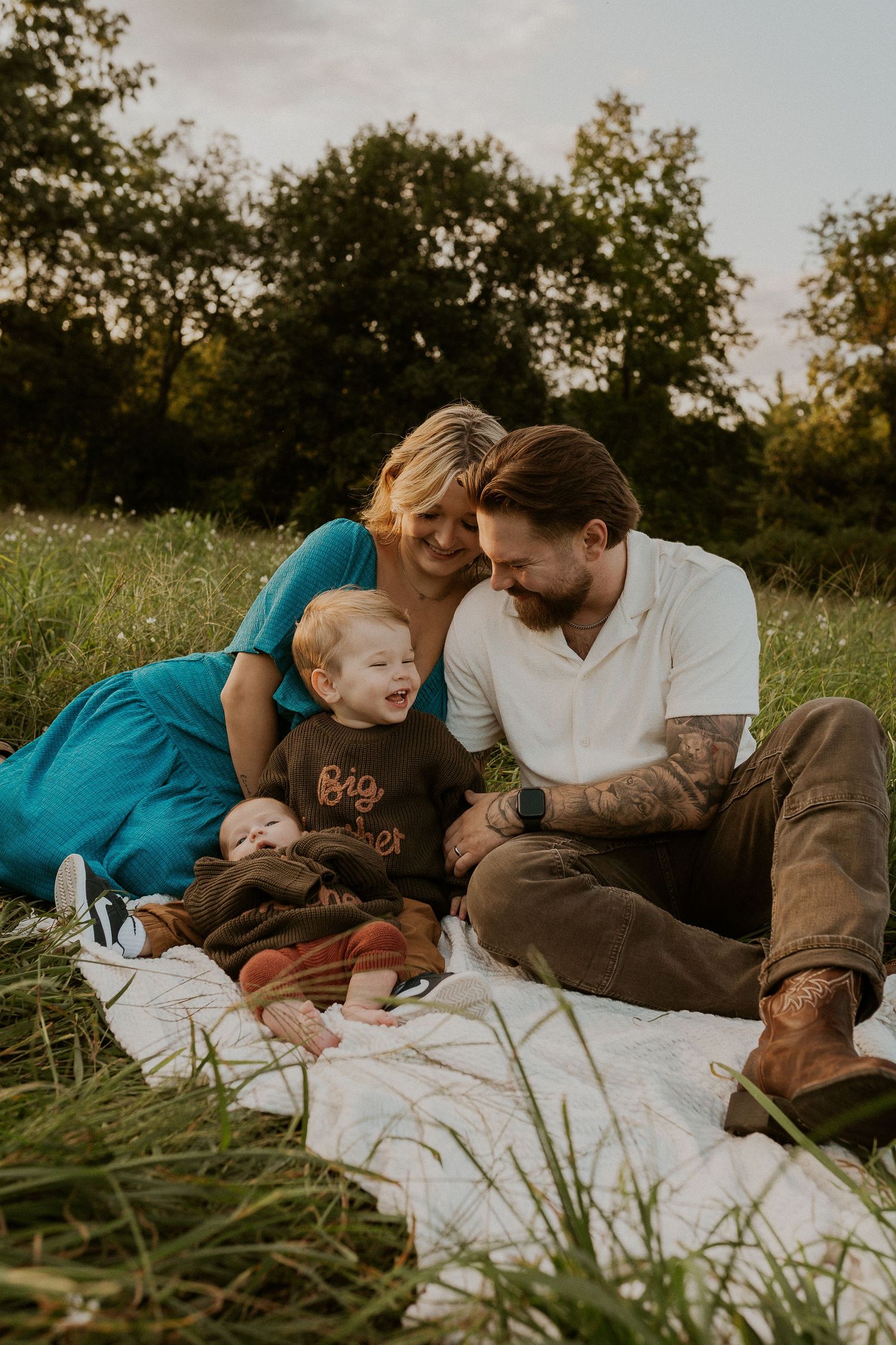 A family shares a joyful moment together on a blanket in a sunlit meadow during golden hour.